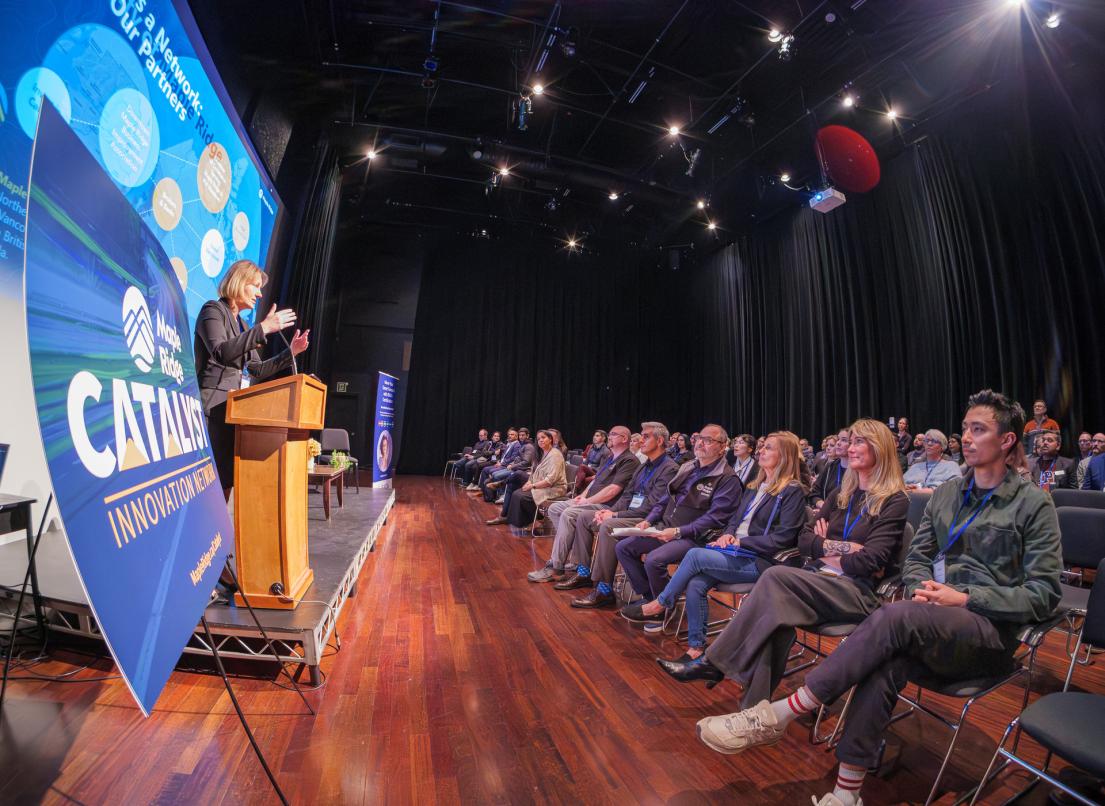 A woman speaks to a large seated crowd in the ACT Studio Theatre.