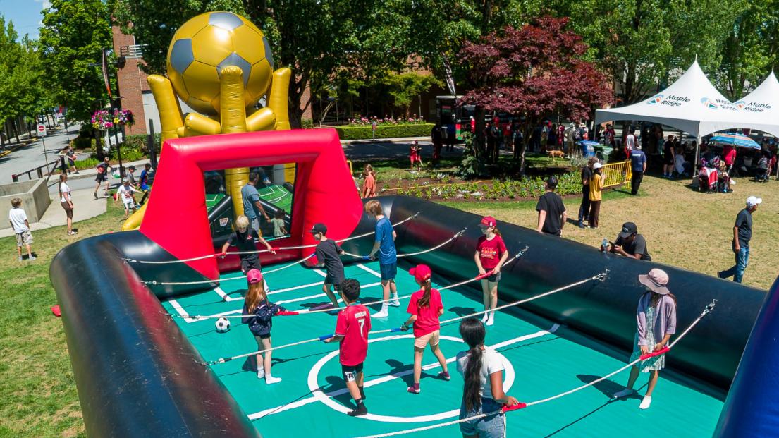 A group of children play human foosball in an inflatable arena.