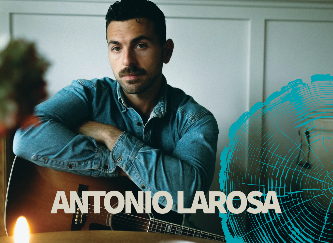 Antonio Larosa looks at the camera while sitting holding a guitar.