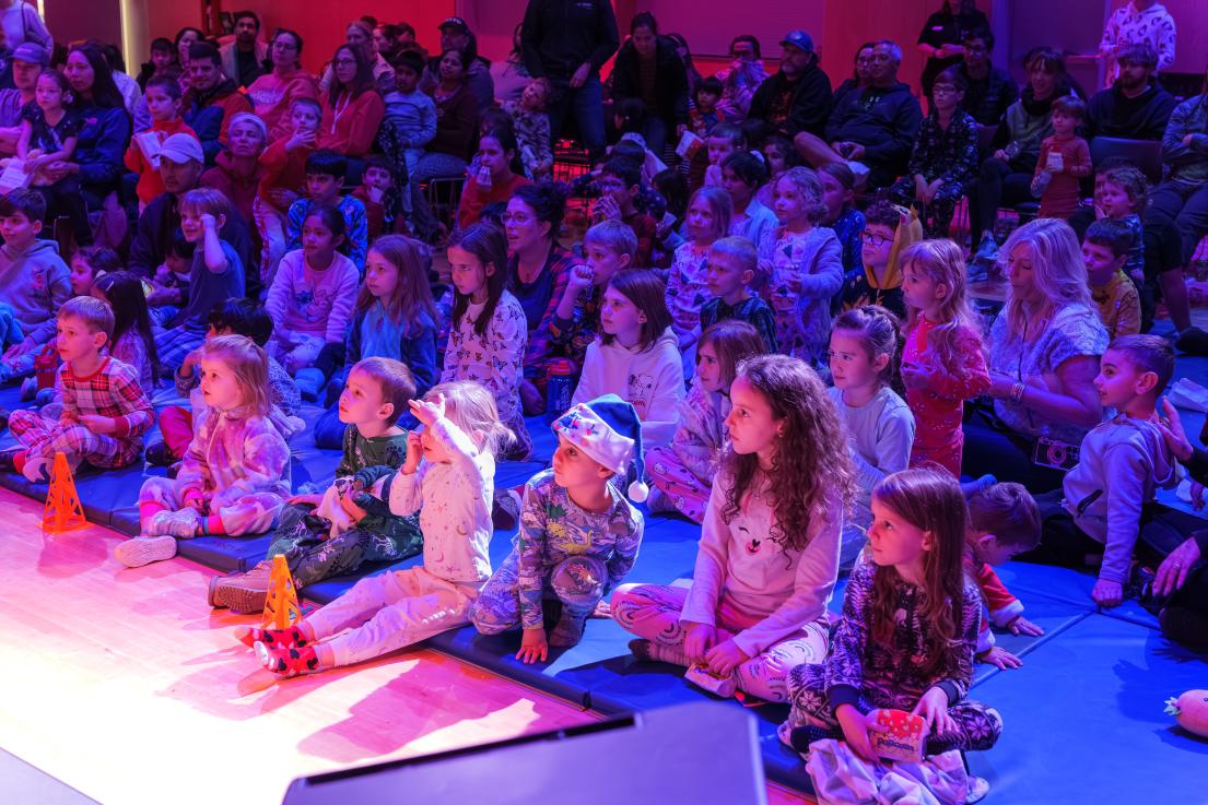 A crowd of kids in pyjamas watches a performer onstage.
