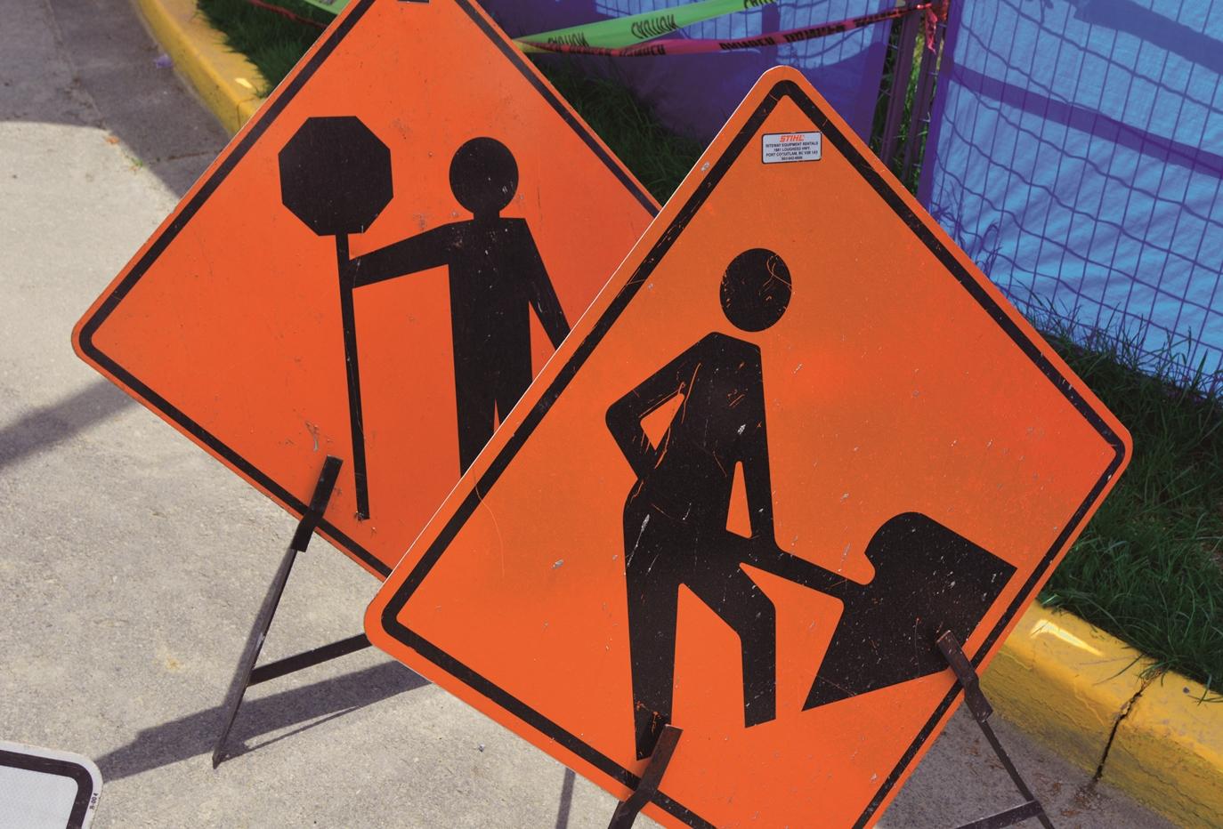 A pair of orange constructions signs: one indicates that there are workers present, while the other warns drivers to be prepared to stop for flaggers.
