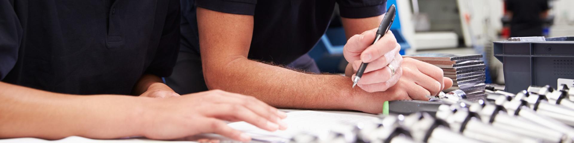 A pair of people in review paperwork, pen in hand.
