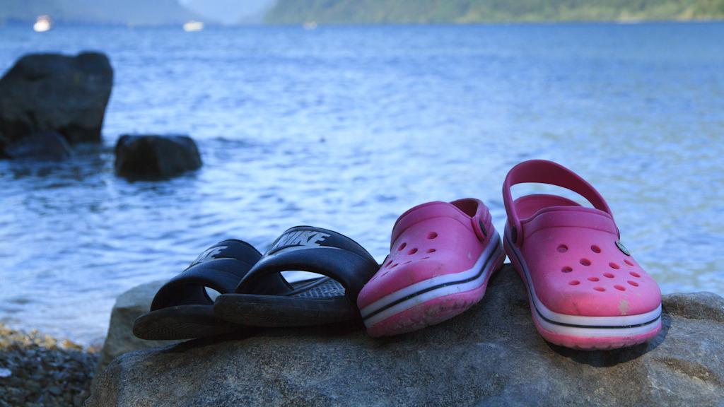 Two sets of sandals sit on the shores of Alouette Lake looking over the water.