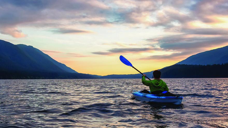 A man lifts half of a kayak oar into the air while paddling across Alouette Lake.