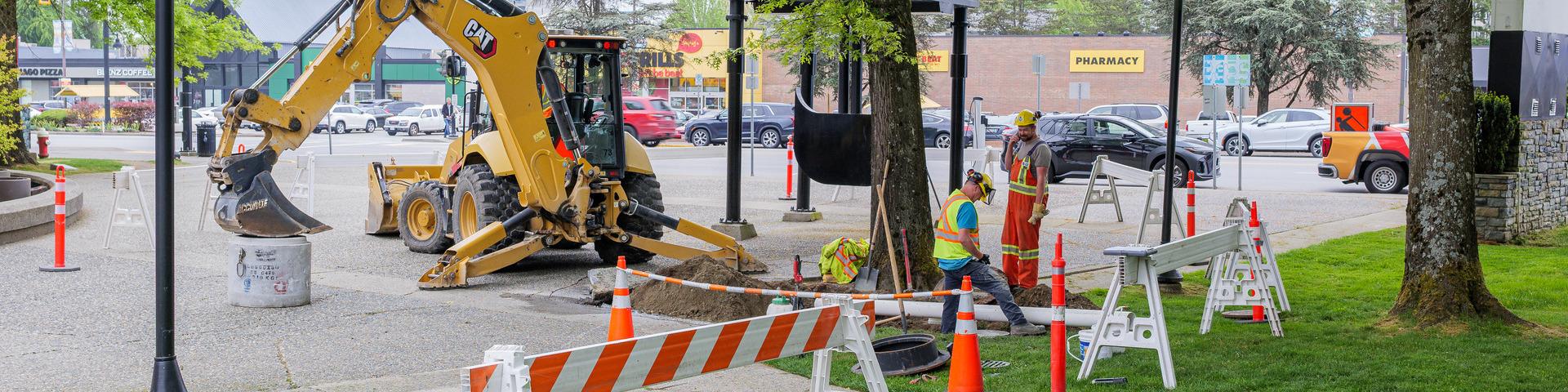City workers replace a pipe using heavy duty equipment under a walkway along Dewdney Trunk Road.