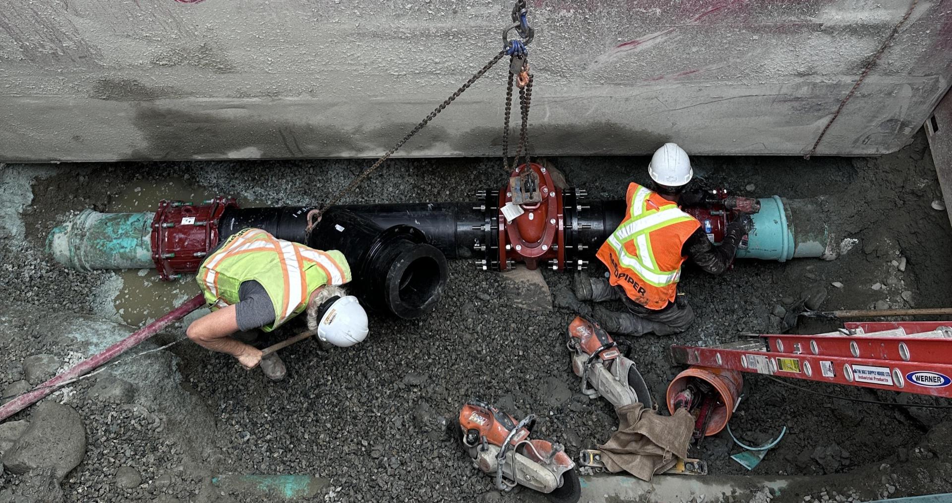 Workers in a trench install a valve on a water pipe