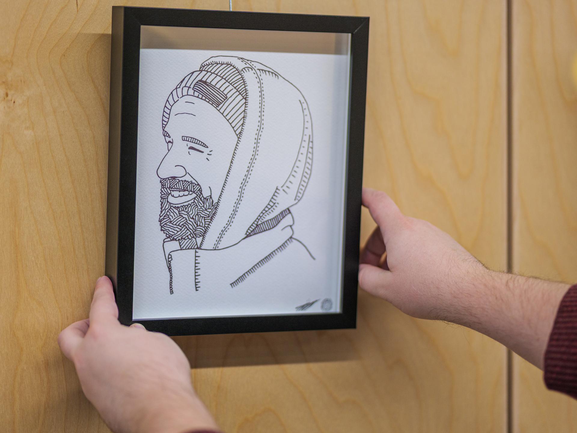 Alex Neff hangs one of many black-and-white line art portraits in their art installation, "Constellation".