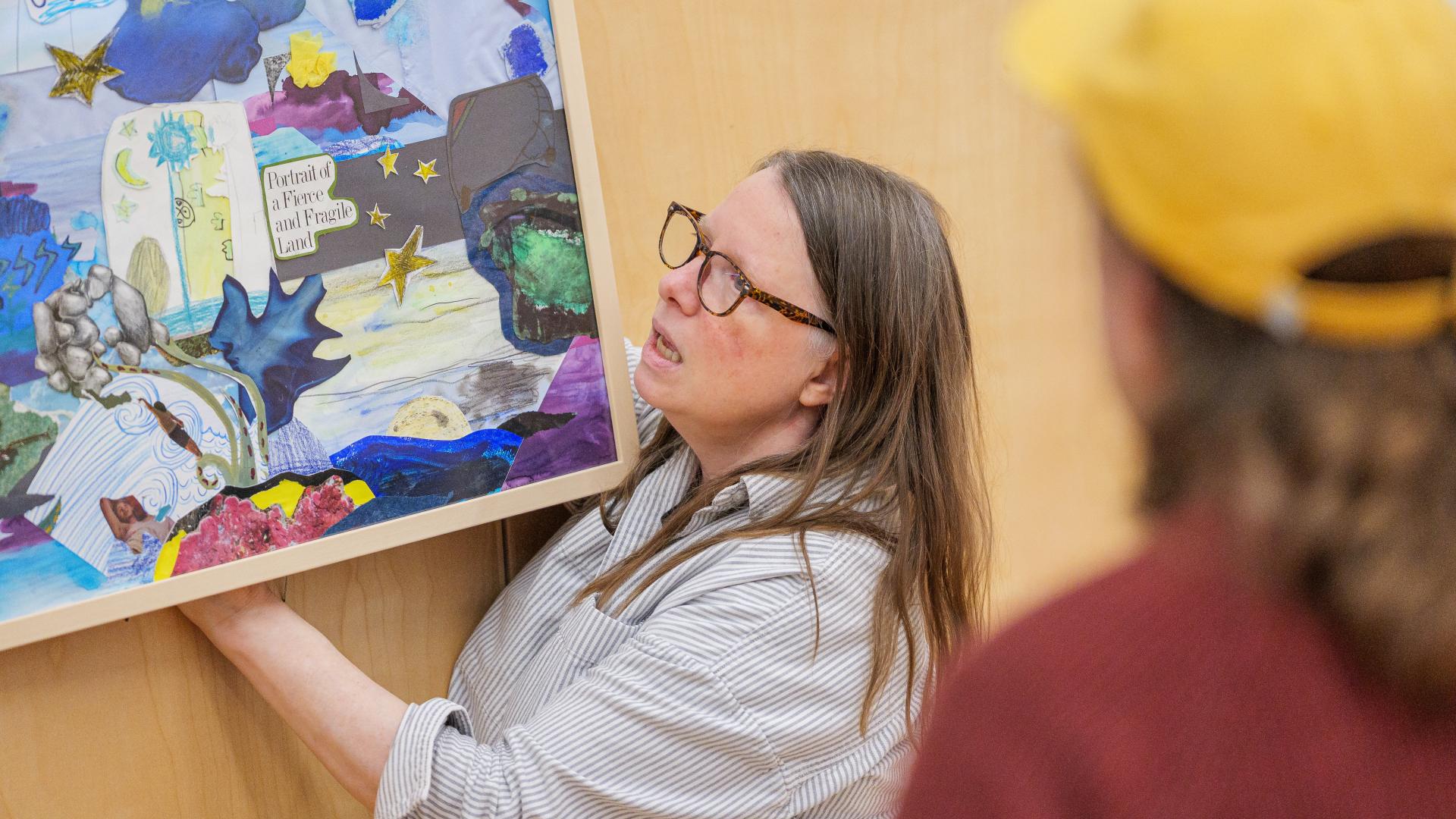 Colleen Brown adjusts a collage on the wall at the Albion Community Centre as Alex Neff watches.