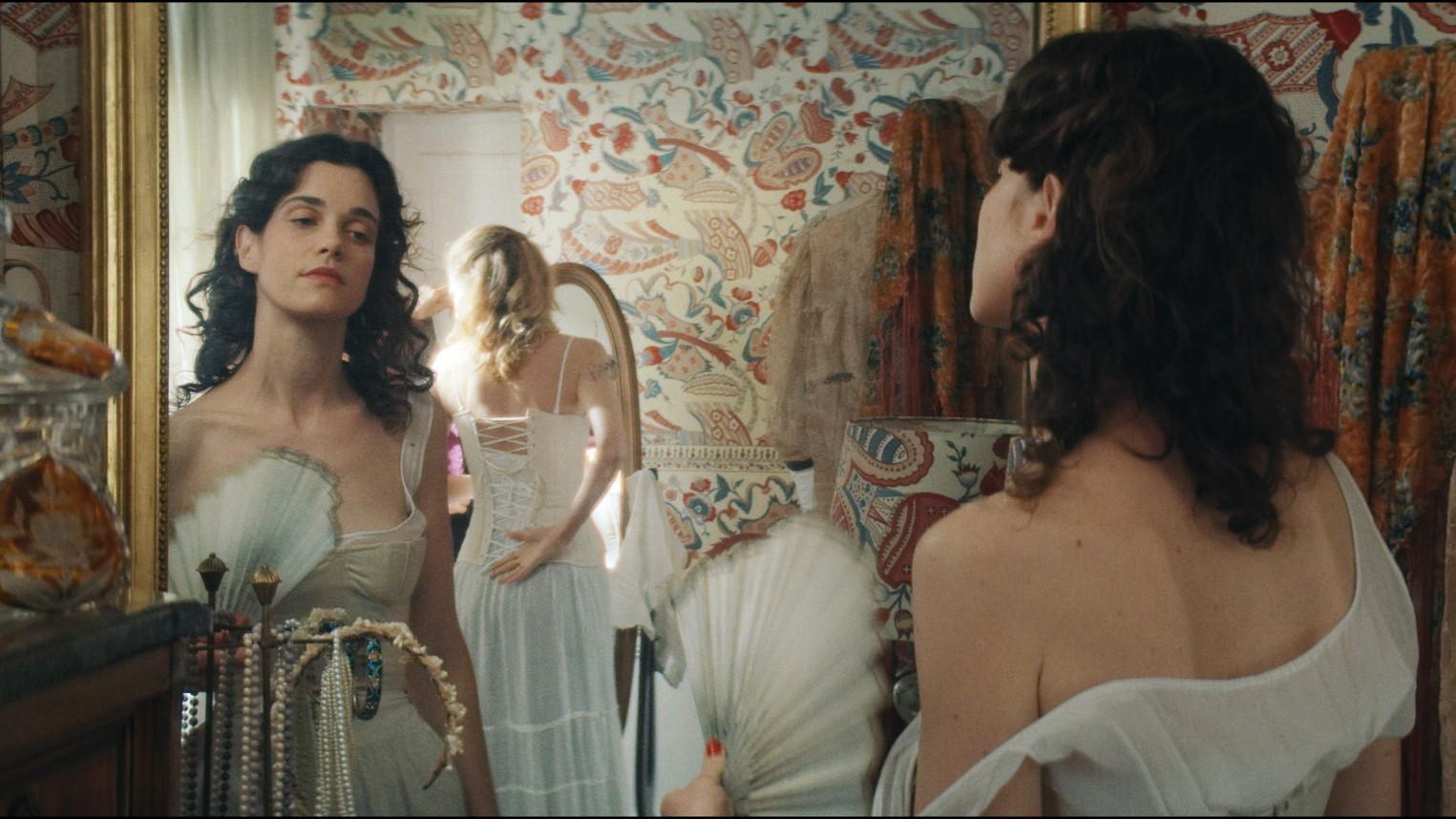 A woman wearing a white ballgown looks at herself in the mirror.