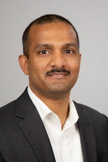 Dr. Jon Thomas wears a black suit against a plain grey background.