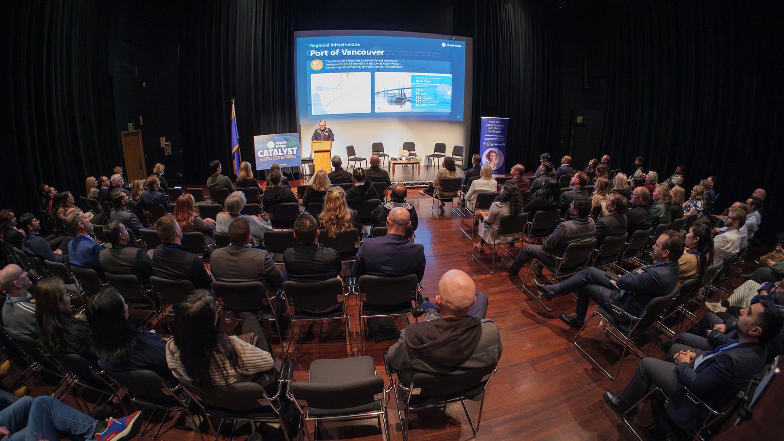 A large crowd watches the presenter in the ACT Arts Centre Studio Theatre. 