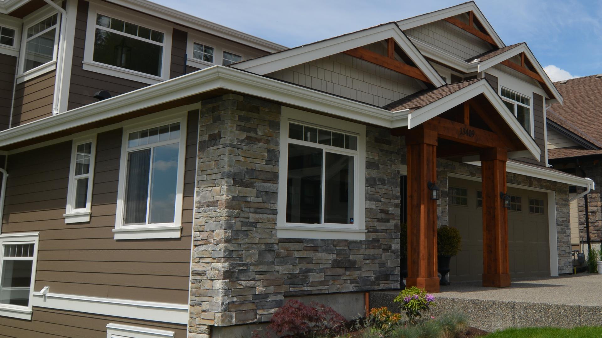 A large brown house with a stonework facade sits at the edge of a driveway.
