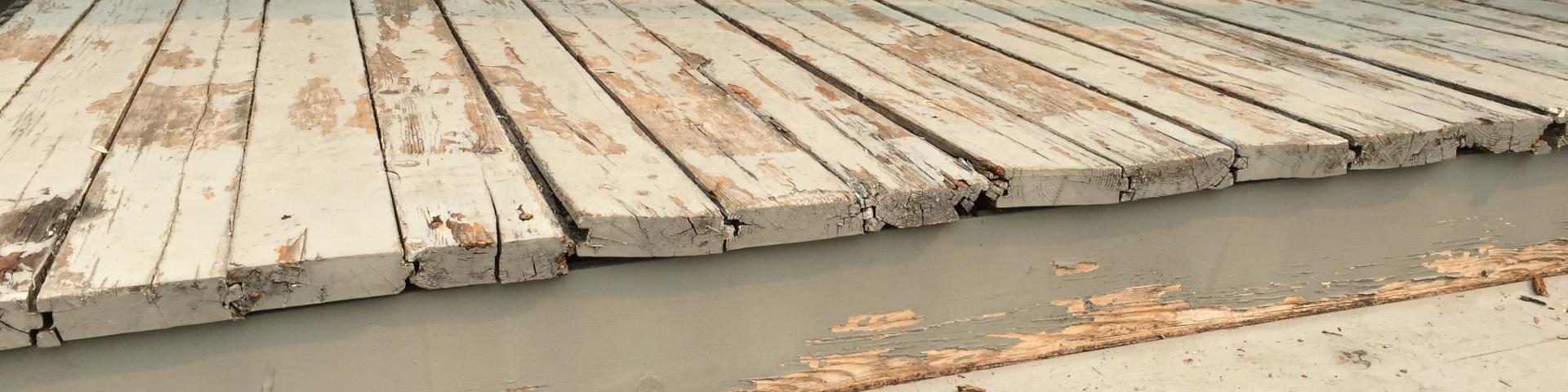 A deck shows its age where grey paint has chipped away to the reveal pale wood underneath.