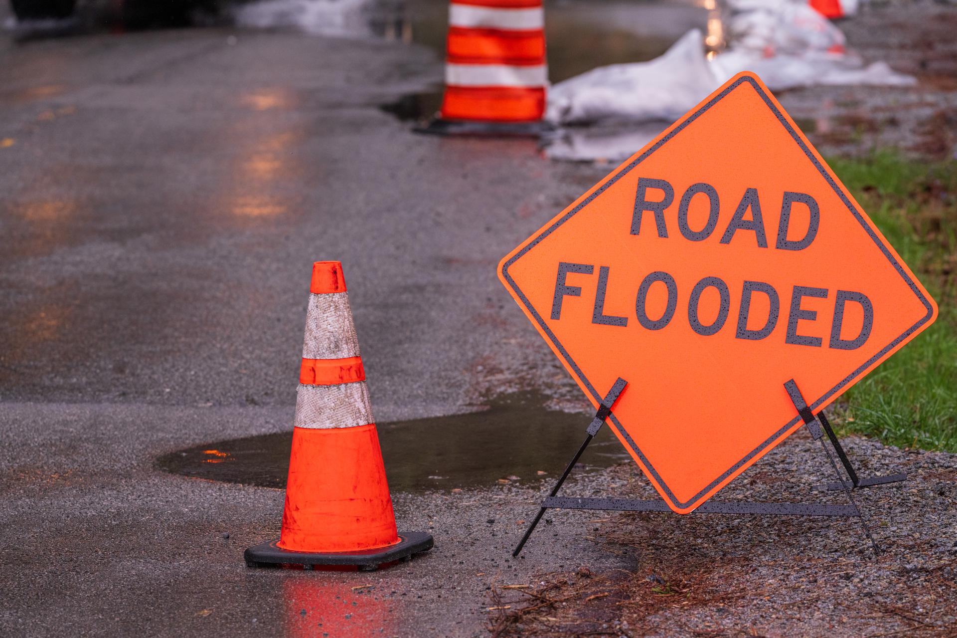 A road flooded sign and traffic cone on a roadway