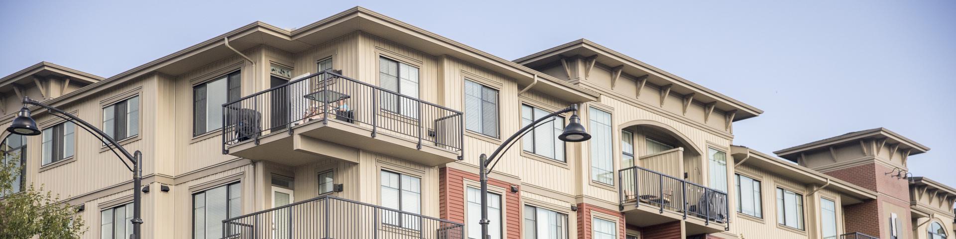 A cream apartment building stands against a light grey-blue sky.