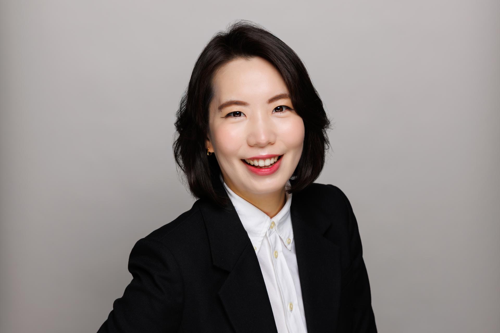 Katherine Kim smiles at the camera wearing a black suit and white undershirt.
