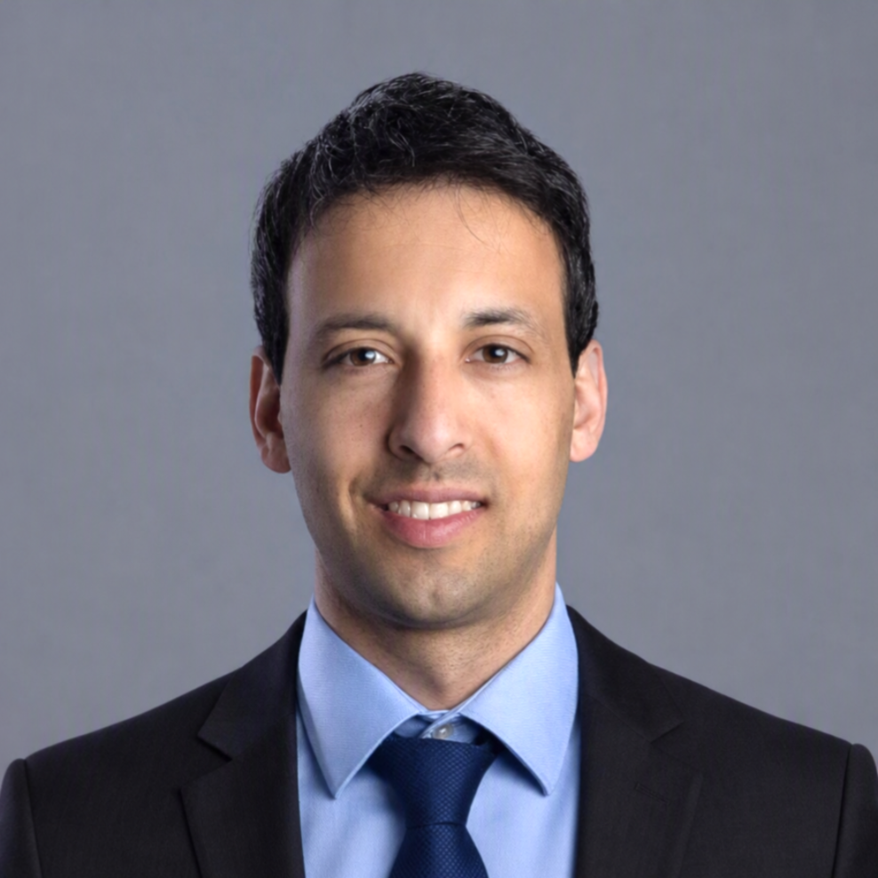 Stephen Millar smiles at the camera wearing a black suit with light blue undershirt and dark blue tie.
