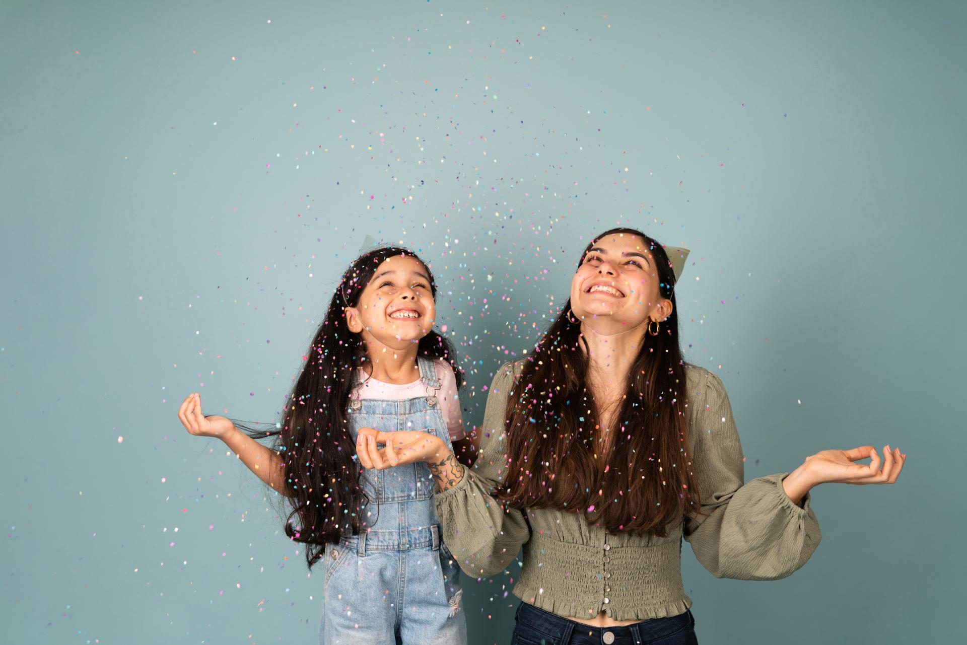 Two young girls look up with glee as sparkly confetti falls on them.