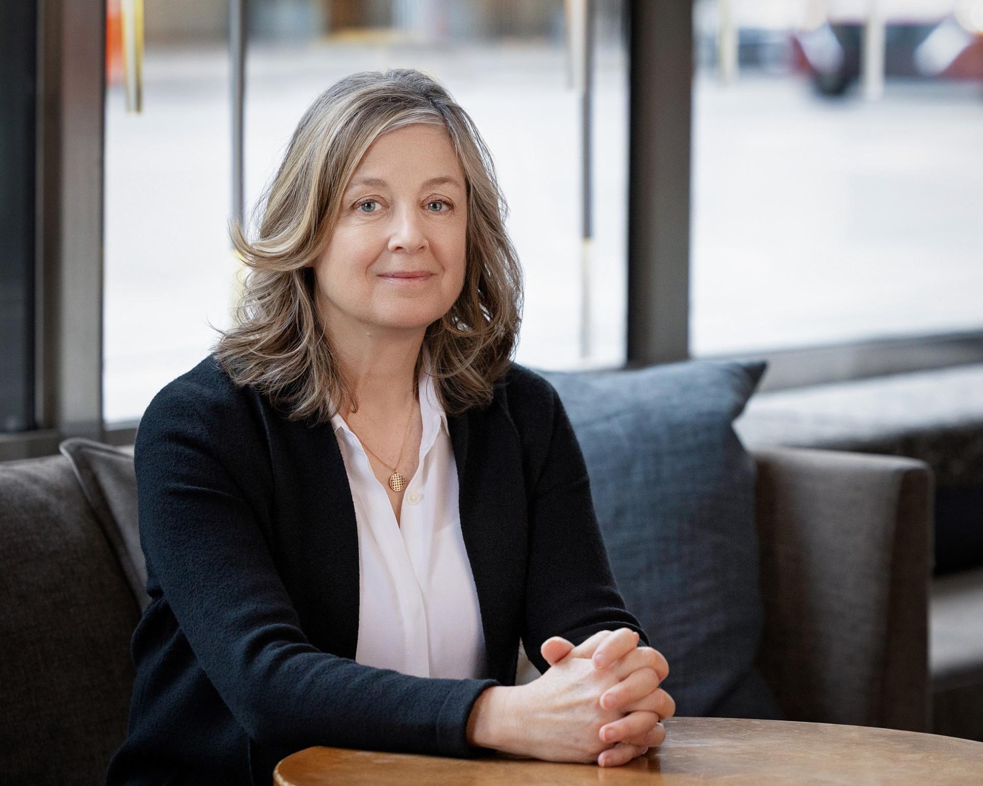 Lori Oliver sits at on a small couch at a table.