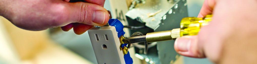 An electrician uses a screwdriver to tighten an electrical plug outlet.