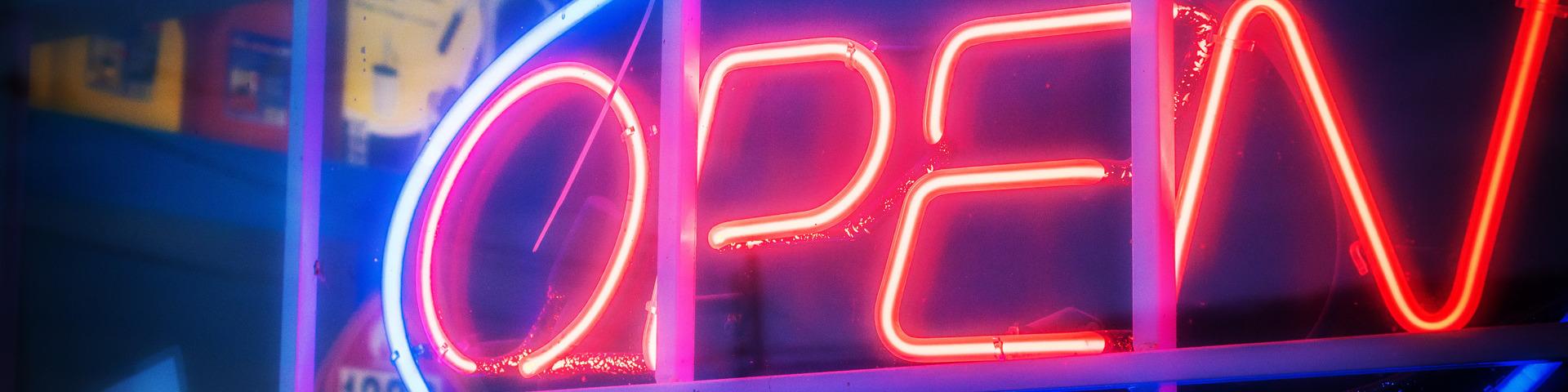 A blue and red neon sign shines "open" through a business's front window.